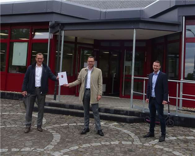 : Bürgermeister Maximilian Mumm und Thomas Häuser (rechts) vom Bauamt der VG Maifeld freuen sich über den von Staatssekretär Dr. Alexander Wilhelm überreichten Förderbescheid für die Maifeldhalle in Polch.