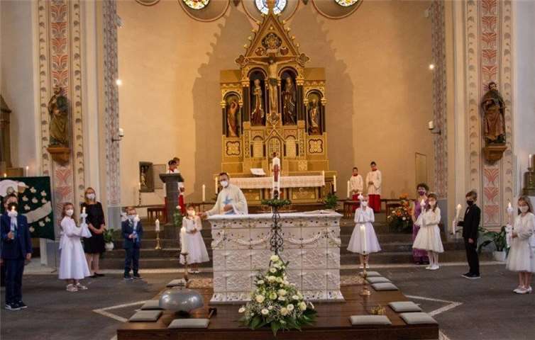 23 Kommunionkinder, die Katechetinnen Nicki Meister und Sabine Lohner, Messdiener und Pfarrer Norbert Missong beim Entzünden der Kommunionkerzen. Foto: privat