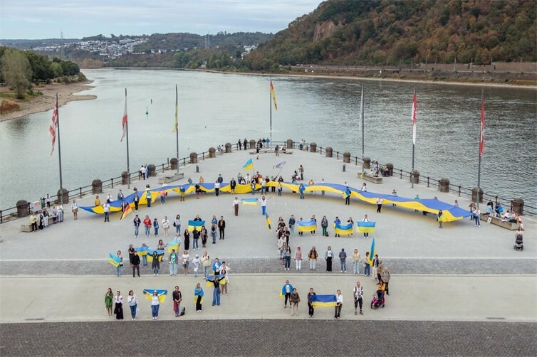 Abschlusskundgebung am Deutschen Eck: Die Teilnehmerinnen und Teilnehmer spannen die Flagge in einer weiten Linie auf dem Vorplatz auf — ein Blick aus der Vogelperspektive.