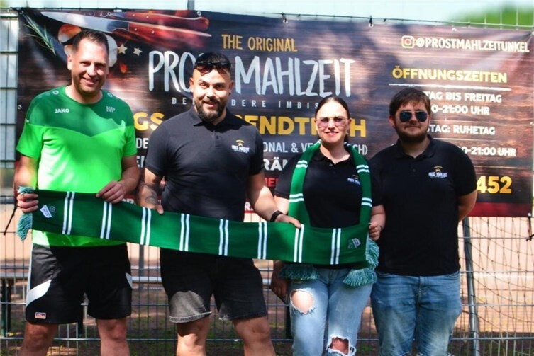Anne Marie Oana, Inhaberin von ProstMahlzeit in Unkel, übergibt die Bande an Niclas Pertzborn (links), Abteilungsleiter Fußball beim SV Leubsdorf.