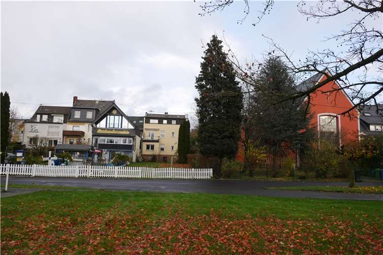 Ansicht von hinten, Rheinanlagen: Mittig ist das abzureißende Drei-Familien-Wohnhaus zu sehen, das direkt an die Ferienpension stößt, auf der anderen Seite an den Kirchgarten der Evangelischen Kirche.