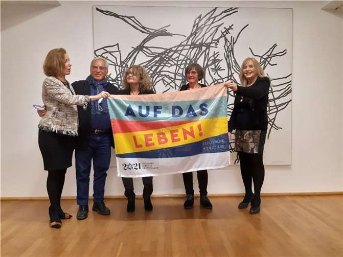 „Auf das Leben!“ V.li. Prof. Dr. Beate Reifenscheid, Direktorin des Ludwig Museums, Dan Sheinman, die Künstlerin Daniella Sheinman, die Vorsitzende des „Freundschaftskreises Koblenz-Petah Tikva“, Hilde Arens und PD Dr. Margit Theis-Scholz, Dezernentin für Bildung und Kultur der Stadt Koblenz, zeigen die Aktionsflagge „1700 Jahre Jüdisches Leben in Deutschland“ anlässlich der Schenkung durch Daniella Sheinman an das Ludwig Museum. Foto: Ludwig Museum Koblenz