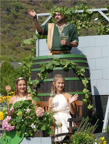 Bacchus Thorsten grüßte das weinfröhliche Volk mit seinen charmanten Bacchantinnen Ronja und Helena vom eigenen Fasswagen.