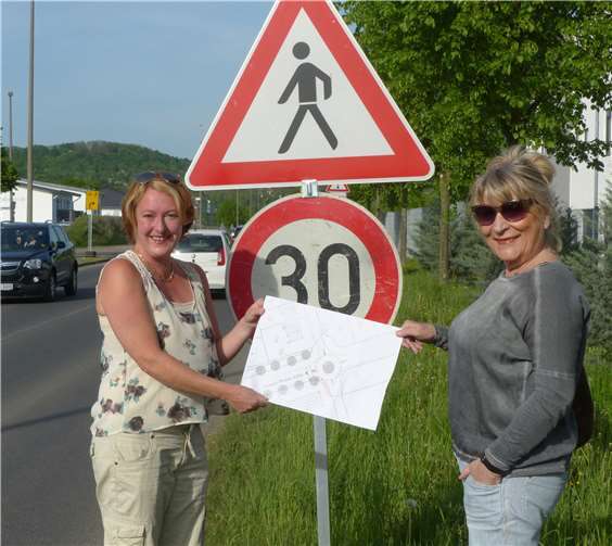 Beate Reich (l) und Christine Wießmann zeigen an der Joseph-Rovan-Allee den Plan für den neuen Verkehrskreisel. privat