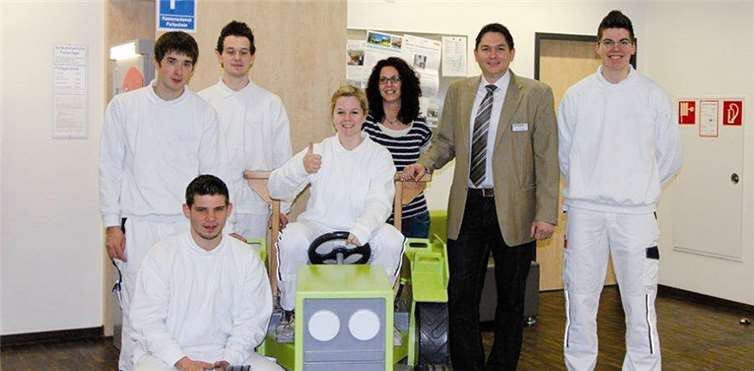 Bei der Übergabe des Holztraktors (v.li.n.re.) li. unten Karl Milke Azubi, li. oben Mathias Schneider Azubi, Niklas Montada Azubi, auf dem Traktor Ricarda Reif Azubi, Frau Muders Bereichsleiterin der Klinik für Kinder- und Jugendmedizin, Herr Radermacher stellvertretender Leiter Gesamttechnik Kemperhof sowie Renè Rübenach Azubi. privat