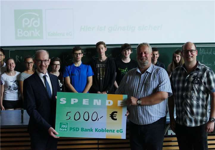 Bernd Schittler (Vorstandsvorsitzender der PSD Bank, l.) überreicht Prof. Peuter Quirmbach von der Universität Koblenz einen symbolischen Scheck im Beisein von Studiendirektor Ruben Keuchel (Max-von-Laue-Gymnasium) und praktikumsteilnehmenden Schülern.  privat