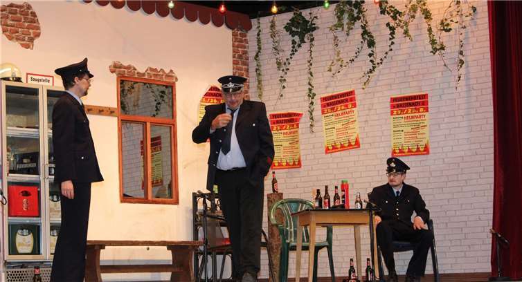 Besorgt machen sich Hauptfeuerwehrmann Harry Pichler (Andreas Barth), Ober-löschmeister Knut Knollenknacker (Werner Willems) und Feuerwehrmann-Anwärter Basti¬an Müller (Kevin Junk) Gedanken um die Nachfolge des verstorbenen Wehrführers.