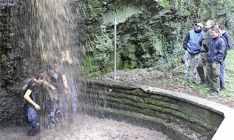 Bibbernd ließen die drei Täuflinge unter dem Wasserfall die übel riechenden braunen Fluten über sich ergießen. DL
