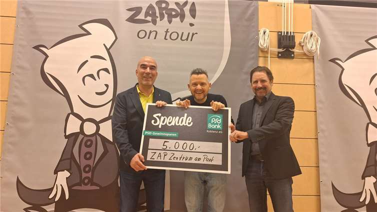 Björn Engelmann, Vorstandsmitglied der PSD Bank Koblenz, Kabarettist Tobias Mann sowie Peter Unkel, 1. Vorsitzender des Kulturkreises Region Emmelshausen e. V. (v.l.n.r.), bei der Übergabe eines Spendenschecks der PSD Bank Koblenz im ZAP in Emmelshausen.  Foto: Thomas Biersch, Kulturkreis Region Emmelshausen e. V.