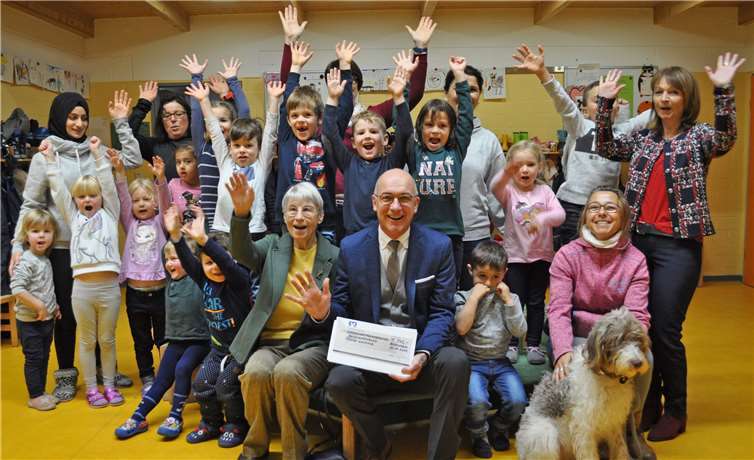 Bürgermeister Bert Spilles, Vorsitzender des Stiftungsvorstands der Bürgerstiftung, und Dr. Erika Neubauer, Mitglied des Stiftungsvorstandes der Bürgerstiftung (in der Mitte sitzend), übergeben den Scheck in der Kita Pusteblume mit ihrer Leiterin Renate Schliebach (rechts stehend). Silvia Johna vom Naturschutzbund (rechts sitzend) freut sich mit den Kindern. Foto: Bürgerstiftung Meckenheim
