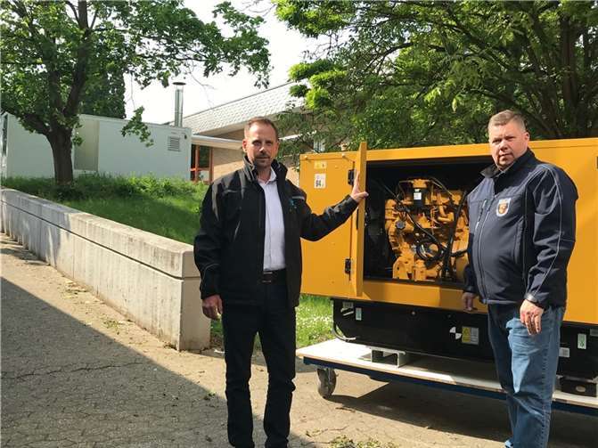 Bürgermeister Björn Ingendahl und Wehrleiter Ingo Wolf vor dem Notstromaggregat. Im Hintergrund die Notheizung für die Rheinhalle.  Foto: Mayk Patella