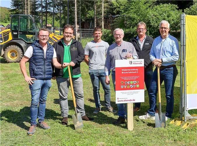 Flut: Erste Brücken an der Mittelahr werden neu gebaut Bürgermeister Dominik Gieler (re.) und Ortsbürgermeister Stefan Zavelberg (3. v. re.) freuen sich, das erste Baustellenschild für drei parallel wiederaufzubauende Fußgängerbrücken aufzustellen. Anwesend waren auch (v. li.) Dennis Schaefer aus der Bauabteilung der Verbandsgemeinde Altenahr, Dipl.-Ing. Jens Heckenbach vom Ingenieurbüro PlannIng, Bauleiter Daniel Wassong sowie Standortleiter Dirk Wassong vom ausführenden Bauunternehmen Knoll. Foto: Thorsten Trütgen / VG Altenahr