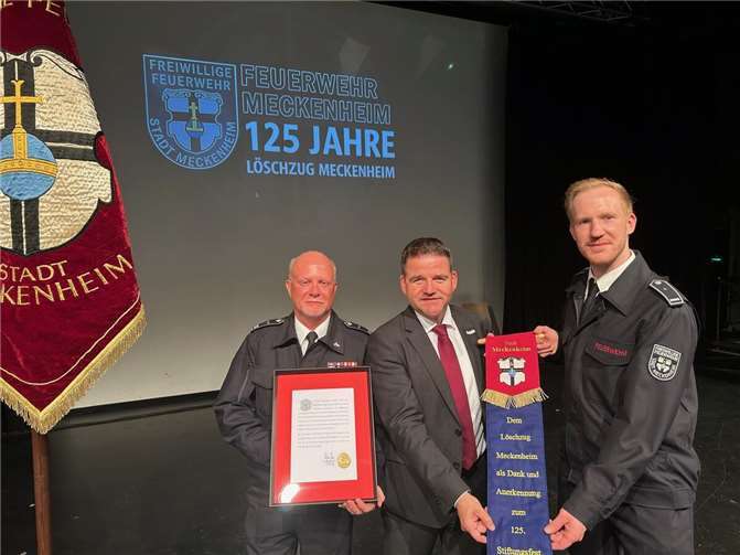 Bürgermeister Holger Jung (Mitte) überreicht die Urkunde und das Fahnenband an Löschzugführer Thomas Rähse (links) und dessen Stellvertreter Adrian Dunkelberg (rechts). Foto: Stadt Meckenheim