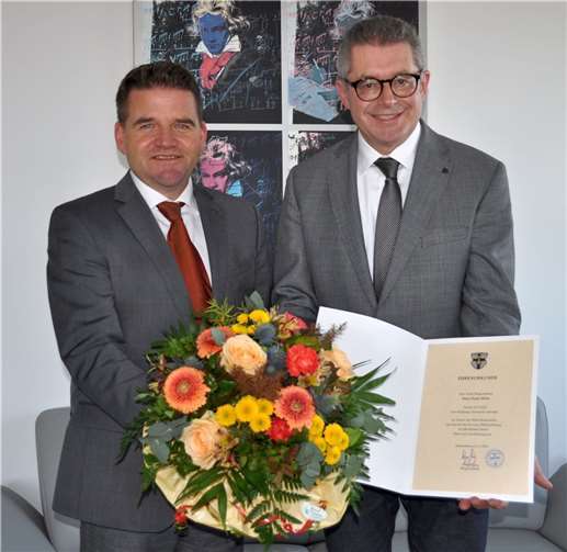 Bürgermeister Holger Jung (links) überreicht dem Ersten Beigeordneten Hans Dieter Wirtz zum Dienstjubiläum die Ehrenurkunde und einen Blumenstrauß.  Foto: Stadt Meckenheim