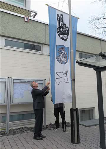 Bürgermeister Jörg Schmidt hisst ein von Jugendlichen gestaltetes Banner mit Wachtberg-Wappen und riedenssymbolen.Foto: Gemeinde Wachtberg/mm