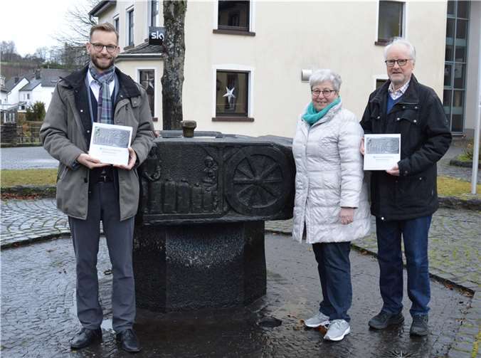 Bürgermeister Ulrich Richter-Hopprich (li) als Herausgeber und die Autoren Eleonore Lenz und Winfried Röther trafen sich am Dorfbrunnen in Niederelbert, um gemeinsam für das Buch „Es klapperten die Mühlen“ zu werben. Der Ort ist nicht zufällig gewählt, denn das Mühlrelief ist auf dem Titel des Buches zu sehen. Foto: VG Montabaur/Ingrid Ferdinand