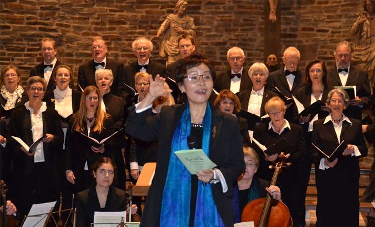 Chorleiterin Sung Ae Park-Kahle (M.) „probt“ mit dem Chor der Versöhnungskirche und dem Kleinen Kammerorchester sowie den Besuchern das gemeinsame Singen. Weigert