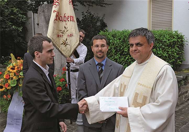 Christian Heinen und Tobias Engels überreichten den aufgerundeten Erlös der Maibaumholzversteigerung an Pastor Peter Dörrenbächer.
