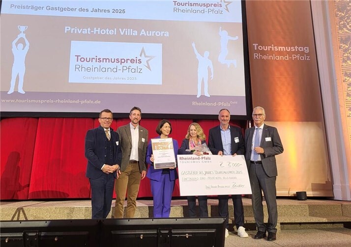 Clarissa und Christian Lindner (3. und 2.v.r.) vom Privat-Hotel Villa Aurora nahmen den Tourismuspreis 2025 von Wirtschaftsministerin Daniela Schmitt (3.v.l.) im Beisein der Jura-Mitglieder RPT-Geschäftsführer Stefan Zindler (2.v.l.), DEHOGA-Vorstand Gereon Haumann (l.) und Arne Rössel von der IHK-Arbeitsgemeinschaft RLP (r.) entgegen.  Foto: Jennifer Hauschild/Rheinland-Pfalz Tourismus GmbH