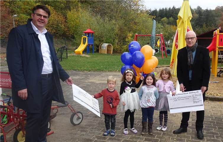 Daniel Probstfeld (li.), Regionaldirektor der Münchener Hypothekenbank) und Udo Link (re.), Vorstand der Raiffeisenbank Welling übergaben die Spendenschecks an die Kinder des Kindergarten Traumland in Trimbs. Foto: privat