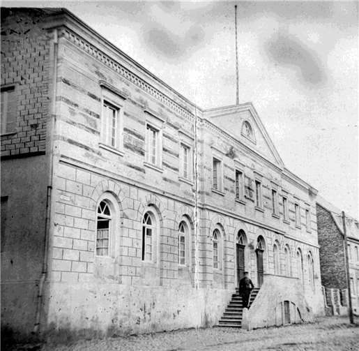 Das 1828/29 errichtete Schulhaus an der Ecke Löherstraße/Am Voigtstor auf einem Foto aus dem Jahre 1878. Im Zweiten Weltkrieg schwer zerstört wurde das Gebäude in der Nachkriegszeit abgerissen.Quelle: Freunde desArchivs der Stadt Rheinbach e. V.