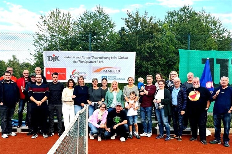 Das Bild zeigt Teilnehmer und Fans vor dem Plakat, womit sich die DJK nochmals bei denSponsoren für die Unterstützung beim Umbau des Tennisplatzes 3 bedankt.