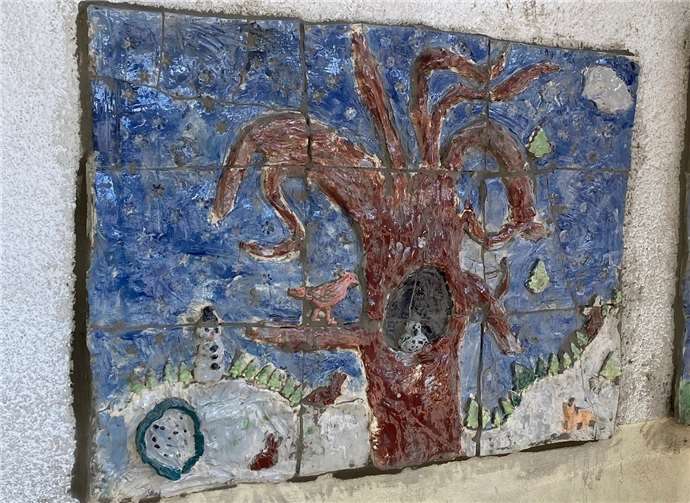 Das Relief zeigt vier Bäume im Wandel der Jahreszeiten und ist aus vielen kleineren, farbig lasierten Tonplatten zusammengesetzt.