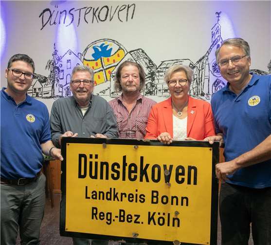 Das alte Ortsschild von Dünstekoven kam nach Hause in den Dorfsaal, wo es künftig einen Ehrenplatz an einer Wand finden wird. Bei der Übergabe freuten sich (von links) KG-Präsident Thomas Nöthen, Wiederentdecker Willi Bregula, Ortsvorsteher Ralf von der Stein, Bürgermeisterin Petra Kalkbrenner und KG-Vorstand Udo Schwennecke. Foto: JOST