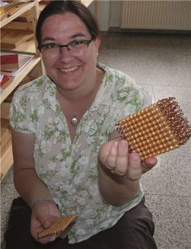 Das goldene Perlenmaterial (hier vorgeführt von Frau Erwen) ist das bekannteste Montessori-Material im Fach Mathematik. Es verdeutlicht durch seine Strukturierung von losen Einzelperlen, Zehnerstäben, Hunderterplatten und Tausenderkuben die Verhältnismäßigkeit im Zahlenraum bis 1000. -FRE-
