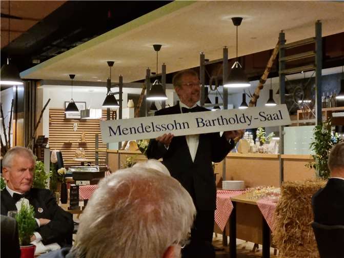 Der 1.Vorsitzende präsentiert den Namenszug des Chores, der für einige Zeit als Türschild über dem Eingang zum Nebensaal der Stadthalle hing.