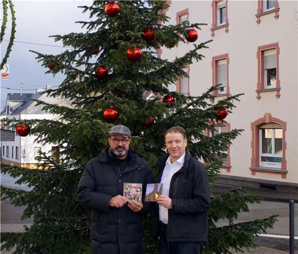 Der Kettiger Ortsbürgermeister Peter Moskopp (links) und Horst Hohn vor dem Weihnachtsbaum, der in diesem Jahr die Grußkarte der Ortsgemeinde ziert. Foto: privat