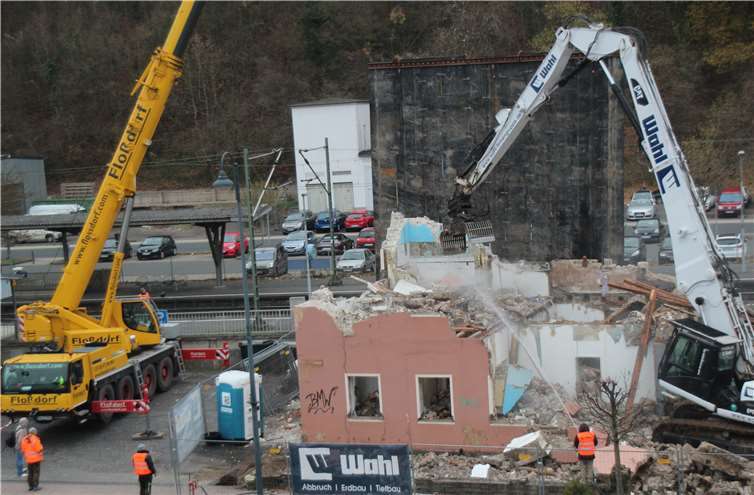 Der Kran links hält die riesige schwarze Gummiabdeckung, die die Gleise und den Bahnsteig mit Fahrgästen vor herabstürzenden Trümmern und Staub schützt, der Bagger rechts führt die Abbrucharbeiten durch.