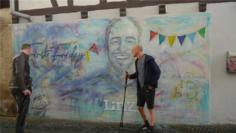 Der Künstler Alexander Wöhrle (rechts) erläutert interessierten Passanten seine „Komposition“, die er zum Motto Straßenkunst am vergangenen First Friday in Linz an seiner Hauswand fertiggestellt hat. Foto: privat