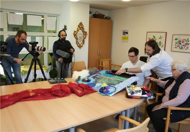 Der Regisseur Volker Maria Engel (2.v.r.) zeigt der Bewohnerin Margarete Heck und Film-Azubi Jonas, wie sie das Fühltuch berühren sollen. Marienhaus Seniorenzentrum St. Josef