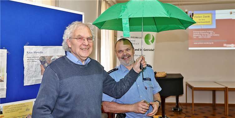 Der Vorsitzende der Rheuma Liga Arbeitsgemeinschaft Adenau, Joachim Keden überreichte ein Glas Honig aus der Jubiläumsedition der Rheuma Liga Adenau damit „der Dienst gelegentlich mal versüßt werden kann“ und einen Regenschirm, denn „die Polizei soll auch selbst gut beschützt sein“.Foto: Werner Dreschers