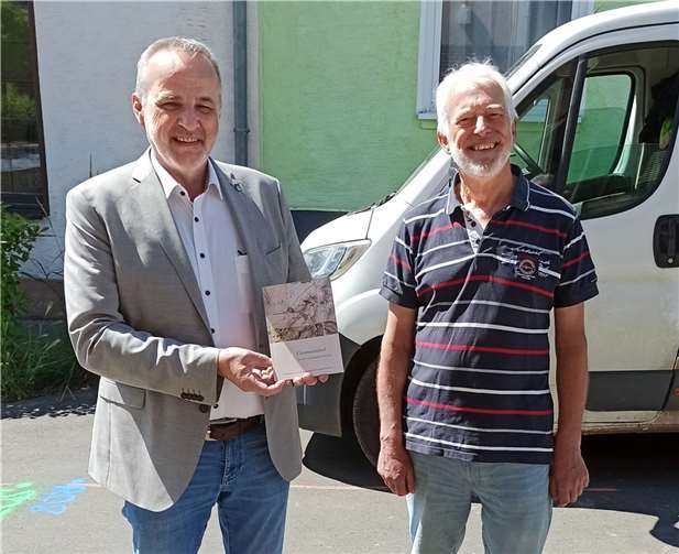 Der Vorsitzende des Bürgervereins „Gimmersdorf Aktiv“ , Frans Bollebakker, übergibt dem Bürgermeister der Gemeinde Wachtberg, Jörg Schmidt, die Erstausgabe der neuen Broschüre über Gimmersdorf’s Historie. Die Aufnahme entstand vor dem Gimmerdorfer Dorfsaal. Hier finden gerade umfangreiche Umbauten für die zukünftige Nutzung im Zuge des „Dorfinnenentwicklungskonzepts“ statt.  Foto: Gimmersdorf Aktiv e.V.