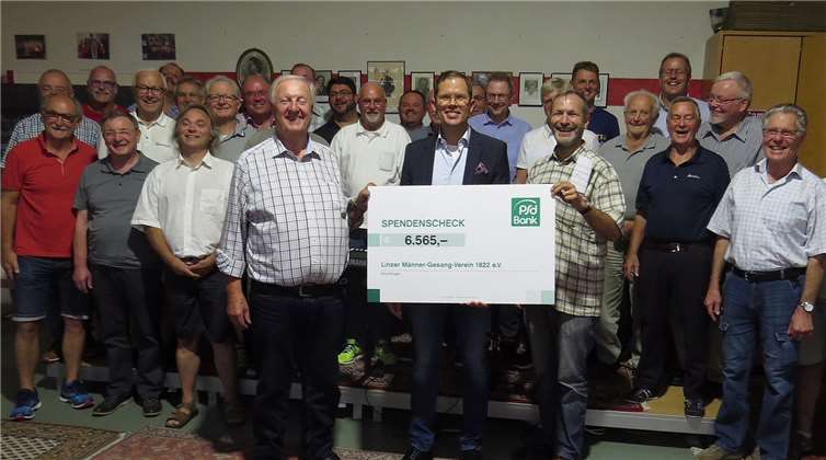 Der Vorstand des Linzer Männergesangvereins Norbert Klein, PSD-Vertriebsvorstand René Königshausen, Dirigent Axel E. Hoffmann und eine Vielzahl der Mitglieder bei der Scheckübergabe im Linzer Sängerheim am Roniger Weg. Roland Thees