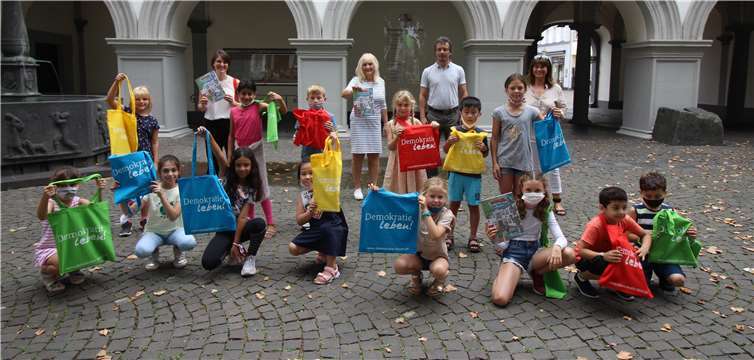 Dezernentin Theis-Scholz (hintere Reihe Mitte) überreicht das Lernmalbuch „Das Rathaus“ stellvertretend an Schülerinnen und Schüler der Klasse 3 b der Koblenzer Grundschule St. Castor mit ihrer Klassenlehrerin Ilse Maluschek-Klee (hintere Reihe rechts) und dem Schulleiter Clemens Haspel sowie Clara Jung vom Schulverwaltungsamt. Foto: Stadt Koblenz