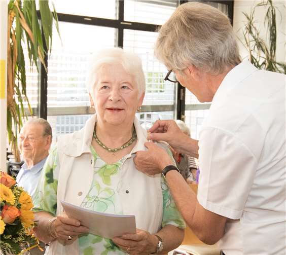 Diakon Michael Lux steckt Barbara Kapol die goldene Caritasnadel an.