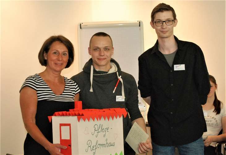 Die Altenpflegeschüler Moritz Höhn (r.) und Florian Kurth übergaben ein „Pflegereformhaus“ mit Anregungen der Altenpflegeklasse an Nicole Westig.