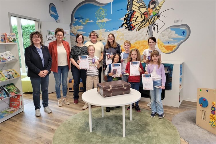 Die Gewinner des Lesesommers 2026: (vorne, v.l.) Amelie (9), Lotta (12+), Lucas-Erich (7), Alexander (10), Ella (8), Mia Sophie (11) und Lea (6) freuen sich gemeinsam mit (hinten, v. l.) Stadtbürgermeisterin Melanie Leicher, Ursula Kingen, Bibliotheksleiterin Carina Senko und Susanne Walter-Hahn über ihre Preise.