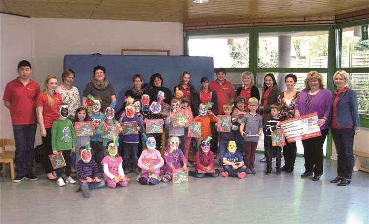 Die Kinder präsentieren ihre selbst gebastelten Masken: KSK-Filialleiterin Claudia Blotzki und Ausbilderin Sabine Birk-Weitzel überreichen einen Scheck an die Kita-Leiterin Sabine Hirsch.privat