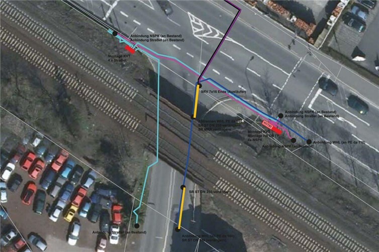 Die Luftaufnahme zeigt: Die Wasserleitung (blau) liegt im Bereich einer Fahrbahn, das Stahlschutzrohr muss für die Aufschüttung der Bahndämme verlängert werden (gelb). Im gleichen Zug werden die alten Kabel für die Straßenbeleuchtung (türkis) erneuert