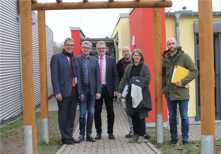 Die Mensa an der Heinrich-Roth-Realschule plus (hinten r.) wird erweitert auf die Fläche, wo derzeit noch ein mit Alu-Blechen verkleideter Klassenraum-Container (l.) steht. An der Umsetzung des Projektes sind beteiligt: (v.l.) der Erste Beigeordnete Andree Stein, Schulleiter Franz-Josef Gerz, VG-Fachbereichsleiter Guido Göbel, die Architekten Konstantin Hartenstein und Sebastian Stahl sowie Projektleiterin Petra Pöritzsch-Jonas von der VG-Gebäudeverwaltung.Foto: privat