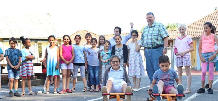 Die Schulleiterin Maria Dehen-Rummel gibt das Startzeichen für die beiden „Testfahrer“ der neuen Gaudi-Flitzer. Die übrigen Grundschulkinder schauen mit großer Erwartung erfreut zu. Fotos: Rita Steindorf