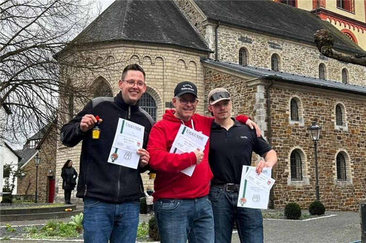 Die Tagessieger im Ostereierkegeln (v.l.): Mario Hänsel (3. Platz), Tom Heck (1. Platz) und Daniel Heck (2. Platz) wurden mit Urkunden und „Erpel-Gutscheinen“ ausgezeichnet – im Hintergrund die Kirche St. Severinus.