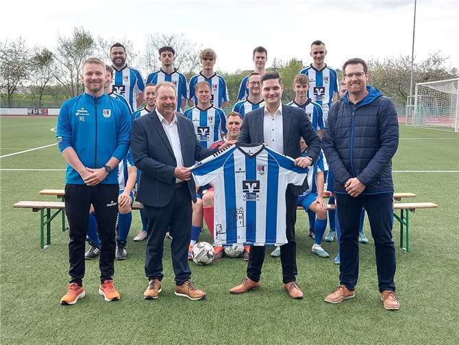 Die VR-Bank RheinAhrEifel eG hat die Fußballsenioren des SV Ochtendung mit neuen Trikots ausgestattet. Die Übergabe der Ausrüstung verfolgte die gesamte Mannschaft (im Hintergrund). Trainer Markus Lenarz (l.) und Vorsitzender Sebastian Neises (r.) dankten dem Leiter der Bankfiliale in Ochtendung, Stephan Flöck, und dem Teamleiter Privatkunden im Regionalmarkt Koblenz, Sören Schlich, (Mitte, v. l.) für die großzügige Unterstützung. Foto: Lothar Kalter