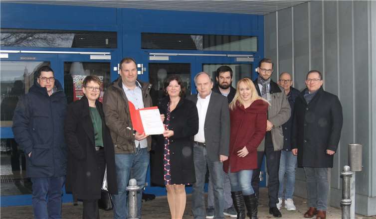 Die Vogelsanghalle in Heiligenroth wird umfassend saniert. Vor dem Eingang trafen sich die am Projekt beteiligten Akteure, als Staatssekretärin Nicole Steingaß aus Mainz den Förderbescheid an Ortsbürgermeister Daniel Kurth übergab. Foto: VG Montabaur