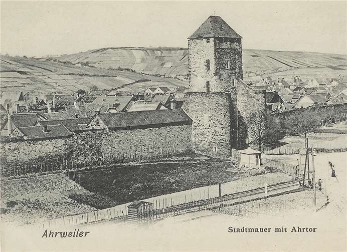 Diese Alte Ansicht zeigt den Platz vor dem Ahrtor. Zu dem Zeitpunkt verlief dort noch die Bahntrasse. Um die Stadtmauer waren noch Gärten angelegt. Etwas versteckt hinter dem Telegrafenmast steht in der Kurve die erste Station des Kreuzweges zum Kalvarienberg. Stadtarchiv Bad Neuenahr-Ahrweiler