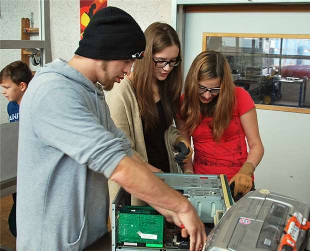 Ein Beschäftigter und Schülerinnen bearbeiten Elektroschrott im Recycling- und Zerlegebereich.